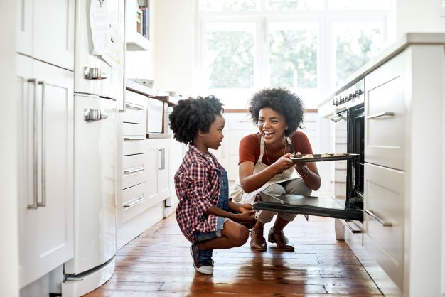 A mother taking baked goods out of the oven as a child watches