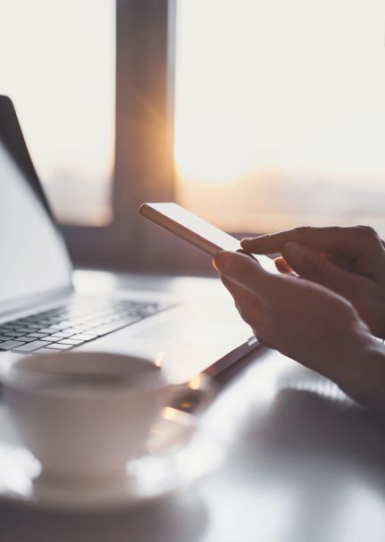 Person scrolling on phone with laptop and tea in background